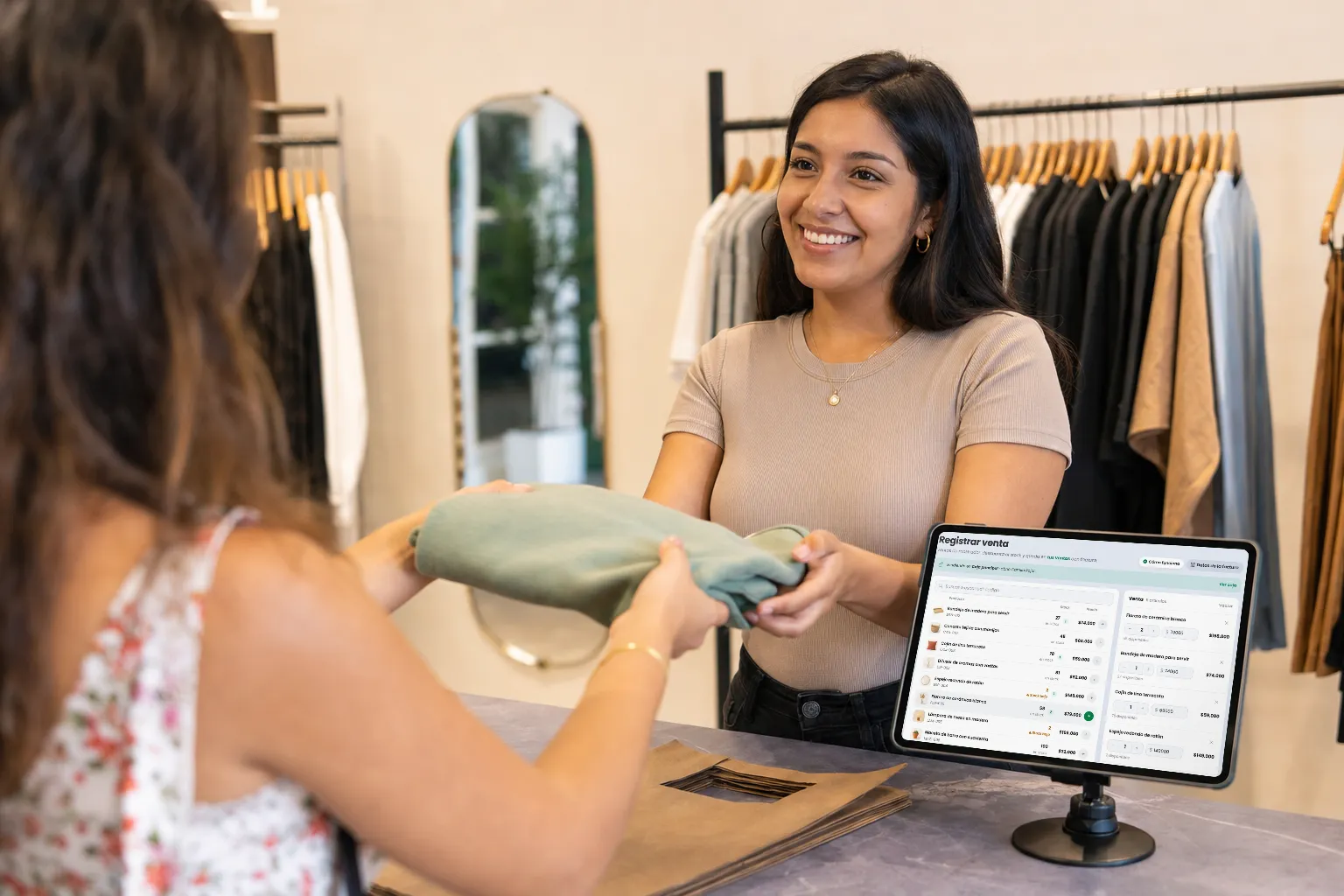 Vendedora de una boutique de ropa entregando una prenda junto a la tablet con el POS de Treggio